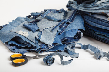 Upcycle old denim garbage. Recycling old jeans. Stack of old blue jeans, cut pieces ready for recycling and scissors on white background. Circular economy. Pile of discarded old blue jeans. Zero waste