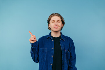 Positive guy in a blue shirt is isolated against the background of a globe wall, looks into the...