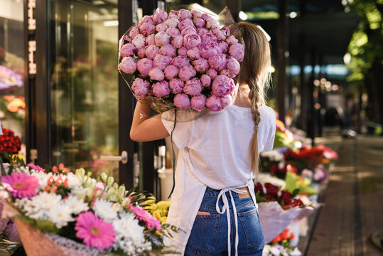 Woman florist with a heap of pink peony flowers in her little flower shop