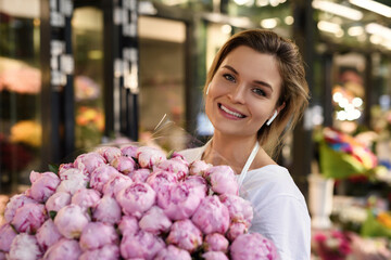 Woman florist with a heap of pink peony flowers in her little flower shop