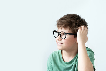 Fototapeta premium Surprised boy in a green T-shirt and glasses pensive scratches his head. Copy space.
