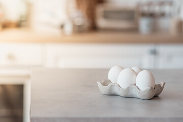 White eggs in a stand lie on a gray concrete table in the kitchen. Sunlight in the corner, Easter card.