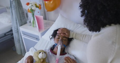 African american mother taking care of her daughter in oxygen mask lying on bed at hospital