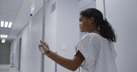 Mixed race girl walking with drip bag in hospital room