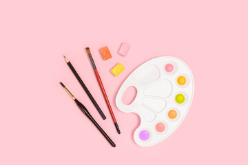 Watercolor palette and paintbrushes on a pink pastel background. Artistic concept.