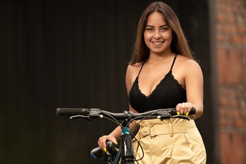 Fototapeta na wymiar Smiling young Hispanic girl with long hair, holding her bicycle.