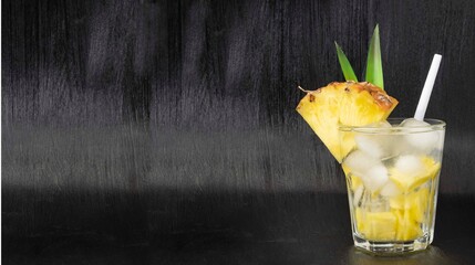 Cocktail in a transparent glass with ice and pineapple on a black background