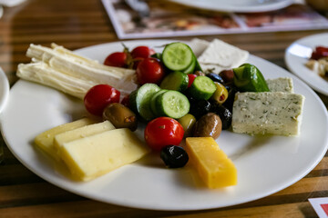 Traditional Turkish delicious breakfast platter on the wooden table with cheeses, olives, vegetables. Close-up view of white plate full of tasty food. Organic, fresh breakfast set. Travel concept.
