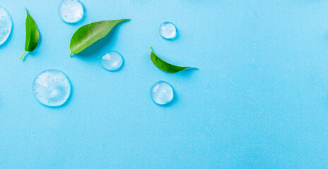 Cosmetics gel and green leaves on blue background. Texture of blue gel or sanitizer. Blue cosmetics gel for face cleansing. Moisturizing, beauty product, lotion, serum for skin care concept
