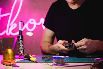 Craftsman holding wire cutters near neon stripe and soldering iron in workshop 