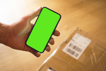 Concept of receiving big parcel at home, smartphone mockup green screen with place for your text for advertising, man hold mobile phone while delivery service shipping parcel box to home door