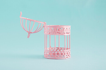 Pink bird cage opened, against pastel blue background. Minimal concept for freedom, unlock,...