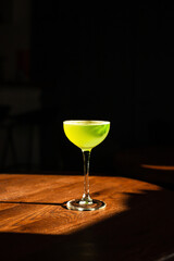 A sweet and sour refreshing basil gin sour cocktail in a coupe glass in direct hard sunlight with long shadows, on a wooden table, vertical photo with copy space