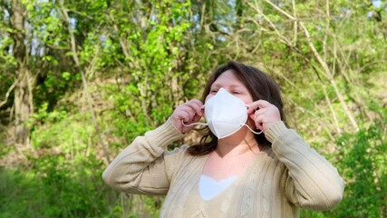 adult European woman 50 years old in beige blouse walks in green park wearing mask, protective respirator with high degree of protection class FFP2, COVID-19 coronavirus in europe, flu, infection