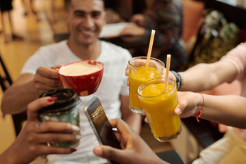 Five hands with glasses of juice, coffee and smartphones, clink glasses, on the background of a wooden table. Cheers