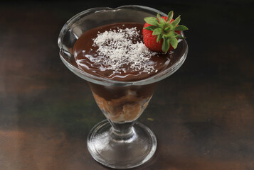 Chocolate pudding in a glass bowl, coconut and strawberries on it. Local name Supangle