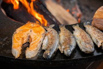 Process of grilling salmon steaks and mackerel fish on black brazier at summer local food market - close up. Outdoor cooking, barbecue, gastronomy, seafood, cookery, street food concept