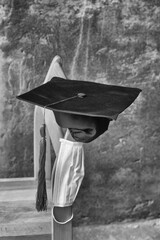 Monochrome composition of graduation day . a graduation hat with medical mask hanging on the chair. Vertical image