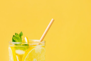 Summer drink with lemon and mint in glass with paper straw on yellow background. Fresh nonalcoholic mojito with exotic fruit and ice. Copy space