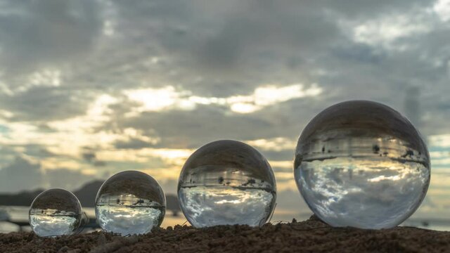 like there are four worlds arranged by size..Four clear glass balls placed on the beach can see the inverted reflection of the sea view in the sunset..A 4K video for a unique and creative travel idea.