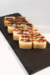 Tempura is a deep-fried sushi roll with prawns, cucumber and cream cheese inside, dressed with sauce and sesame seeds, on a white plate. Japanese sushi food.