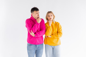 Disappointed young couple in color pullover standing with arms folded over white wall