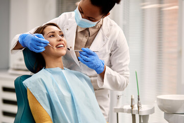 Smiling woman getting her teeth checked during dental appointment at dentist's office. - obrazy, fototapety, plakaty