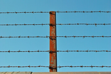 Rusty Steel Fence Post with Barbed Wire Strands against Blue Sky
