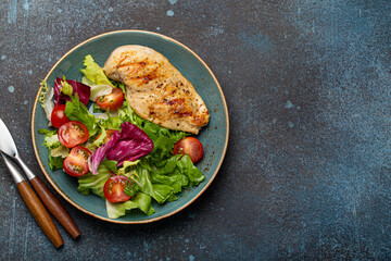 Grilled chicken breast fillet with vegetables salad of fresh tomatoes and salad leaves on blue...