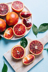 Composition of whole and sliced blood oranges in a plate on light blue table background. Flat lay,...