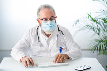Doctor in white coat with face mask while working telematically in his office