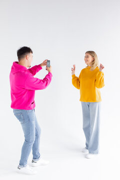 Image of a man take photo of his positive optimistic woman on white background by mobile phone.