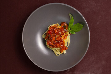 Top view of dish or gray plate with pasta or fettuccine with red or tomato sauce, bacon, pepperoni or calabresa and basil