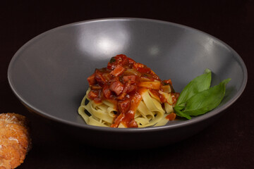 Top view of dish or gray plate with pasta or fettuccine with red or tomato sauce, bacon, pepperoni or calabresa and basil