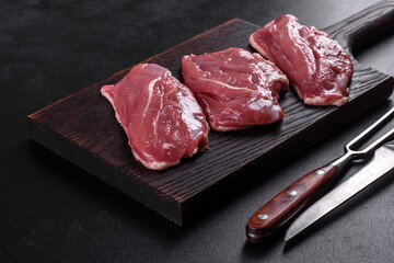 Raw duck breast with herbs and spices on a dark concrete background