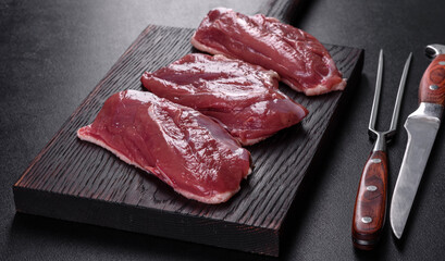 Raw duck breast with herbs and spices on a dark concrete background