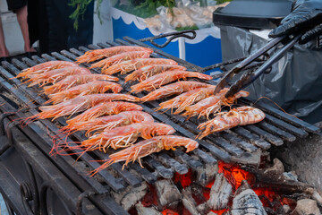 Chef cooking fresh red langoustine shrimps, prawns on grill at summer local food market - close up. Outdoor cooking, barbecue, gastronomy, seafood, cookery, street food concept