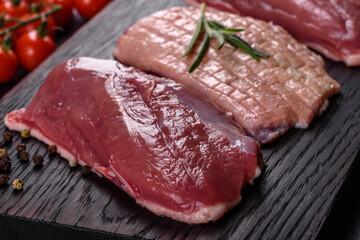 Raw duck breast with herbs and spices on a dark concrete background