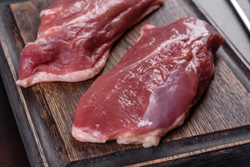 Raw duck breast with herbs and spices on a dark concrete background