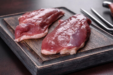 Raw duck breast with herbs and spices on a dark concrete background