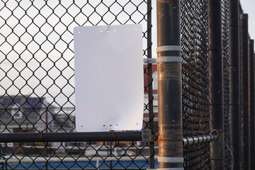 Blank white sign on a metal chain link fence by a playground