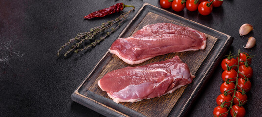 Raw duck breast with herbs and spices on a dark concrete background