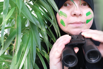 close-up curious islamic woman in war paint, holding field binoculars with zoom, peeping from the...