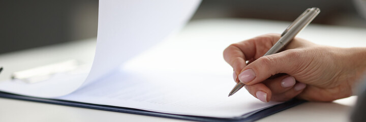 Woman writing with ballpoint pen in documents on clipboard in office closeup