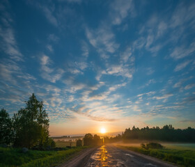 Morning landscape with road passing through field at sunrise.