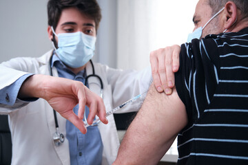 Doctor vaccinating mature man patient in clinic. Nurse holding syringe before inject Covid-19 or...