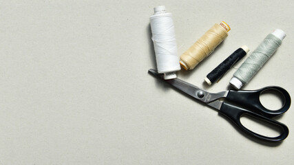 Fototapeta premium Nähgarn in verschiedenen Farben, weiß, beige, schwarz,grau und bereitgelegter Schere auf grauem Hintergrund.