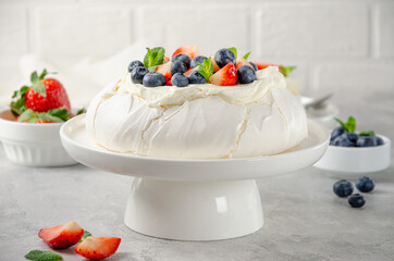 Pavlova meringue cake with whipped cream and fresh berries on top on a plate on a gray concrete background. Summer dessert. Copy space.