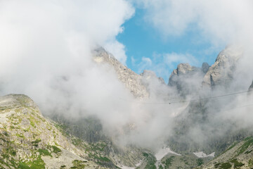 Panoramic view of rocky mountains covered with fluffy clouds. 