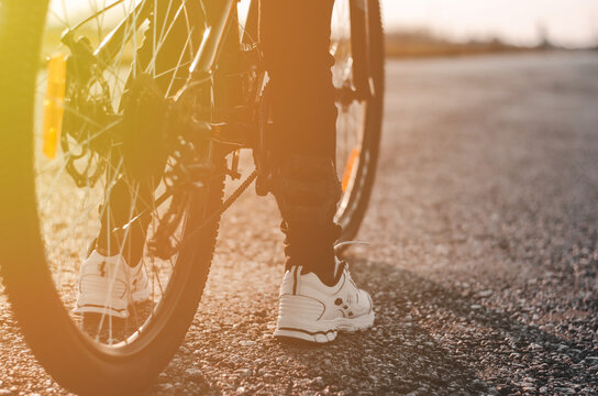 Close-up of bicycle wheels and legs on an empty road. Rear view of a cyclist in the evening sun. Healthy lifestyle concept